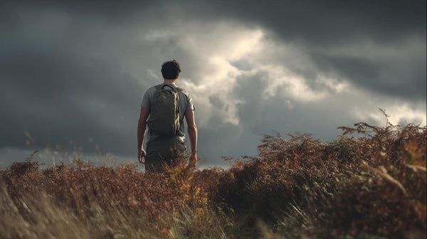  Hiker pausing on Peak District moorland trail wearing a plain cotton t-shirt, overcast sky with patches of light breaking through, heather and bracken in muted autumn