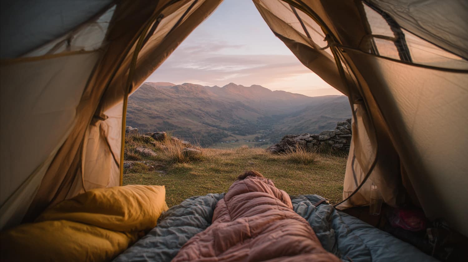 Camper in their tent lying in their sleeping bag at a Lake District campsite in early evening light
