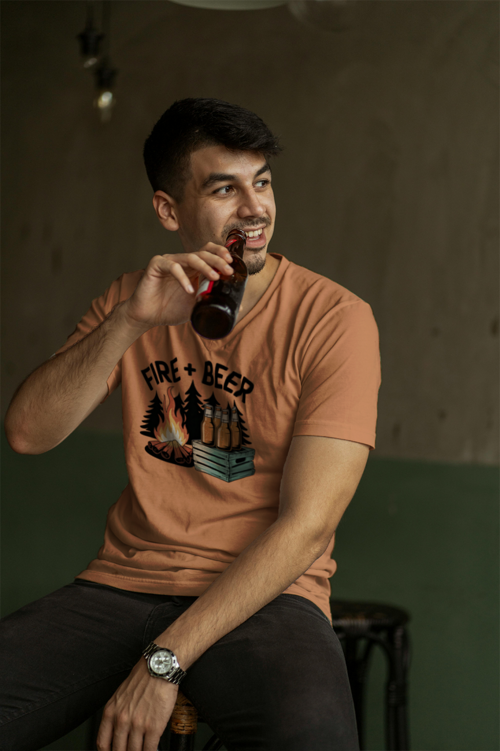 Man wearing a t-shirt with 'Fire & Beer' design, holding a bottle, sitting against a dark background.