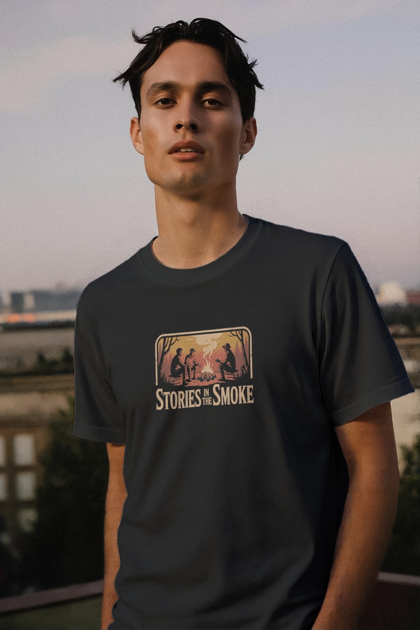 Man wearing a t-shirt with 'Stories in the Smoke' graphic design outdoors.