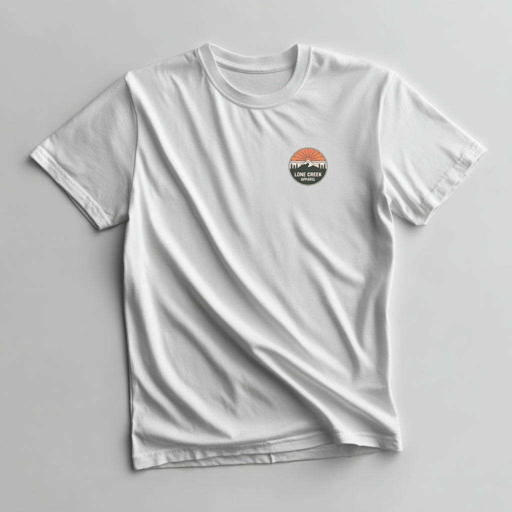 Circular mountain badge graphic in dark green, orange, and cream with Lone Creek Apparel text on a White graphic tee