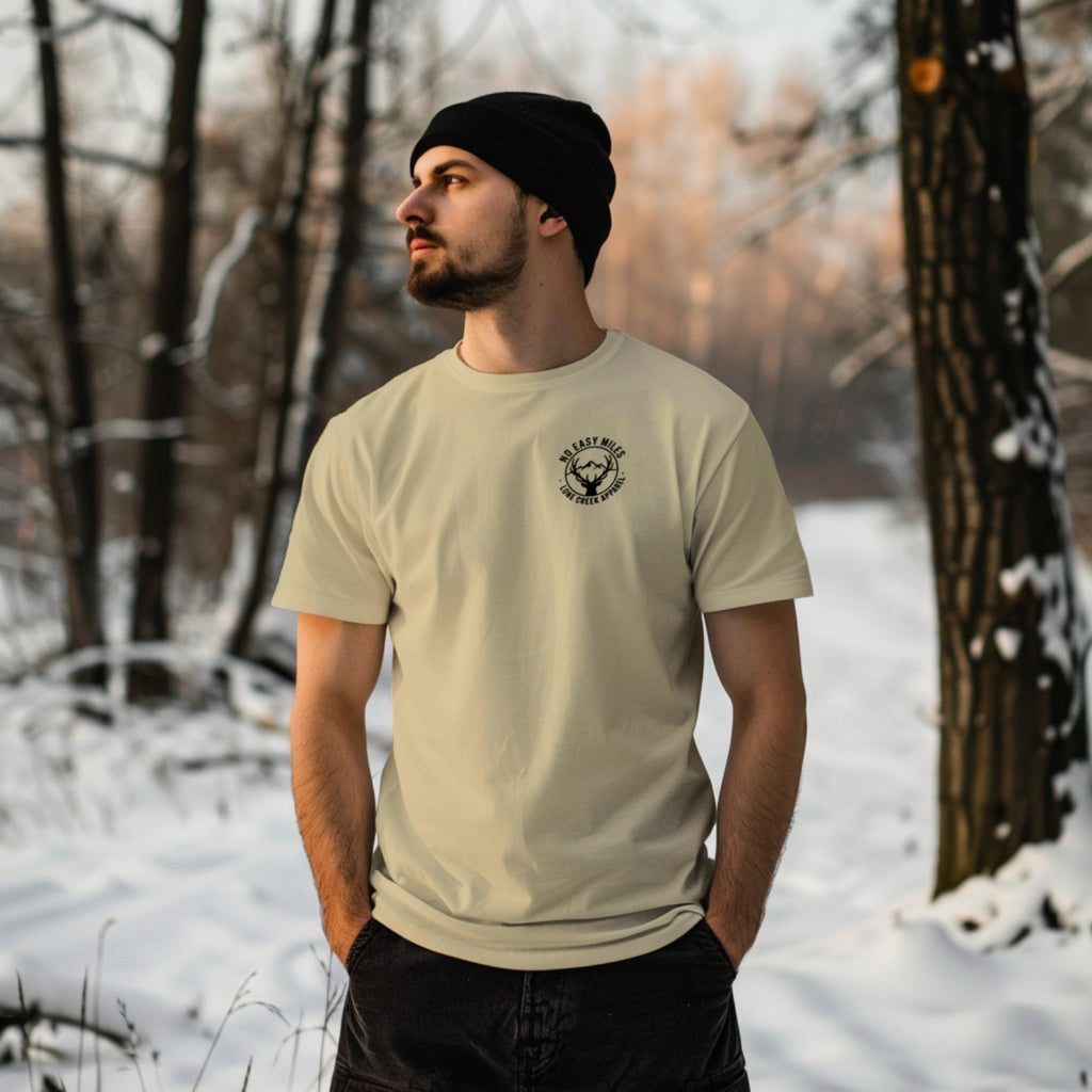 Man wearing a beige t-shirt with a logo in a snowy forest