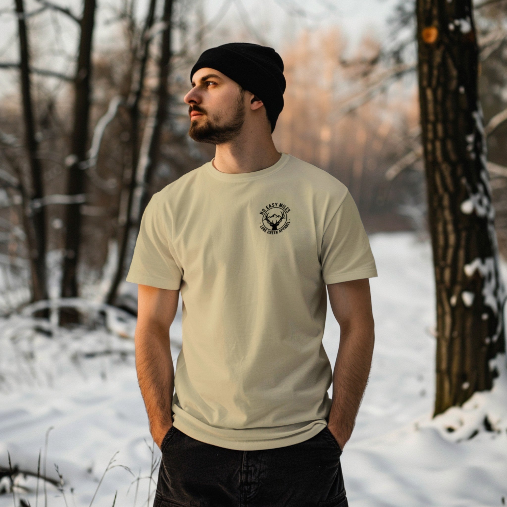 Man wearing a beige t-shirt with a logo in a snowy forest
